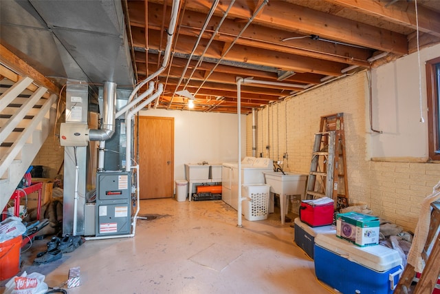 unfinished below grade area featuring washing machine and dryer, heating unit, a sink, and brick wall