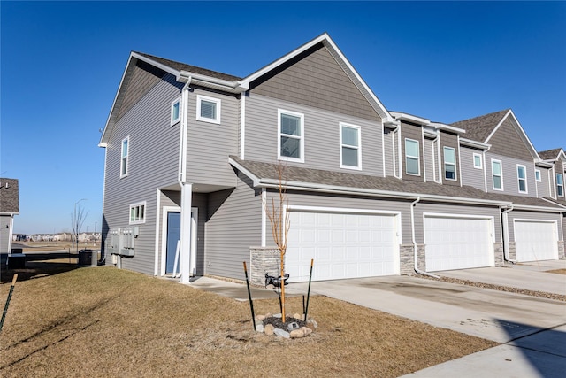 townhome / multi-family property with central AC unit, an attached garage, a shingled roof, stone siding, and driveway