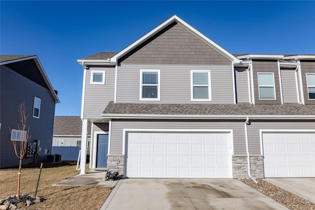 townhome / multi-family property featuring stone siding, concrete driveway, central AC, and roof with shingles