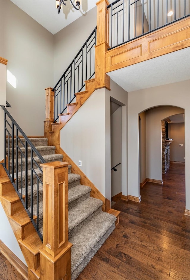 stairway with arched walkways, a towering ceiling, baseboards, and wood finished floors