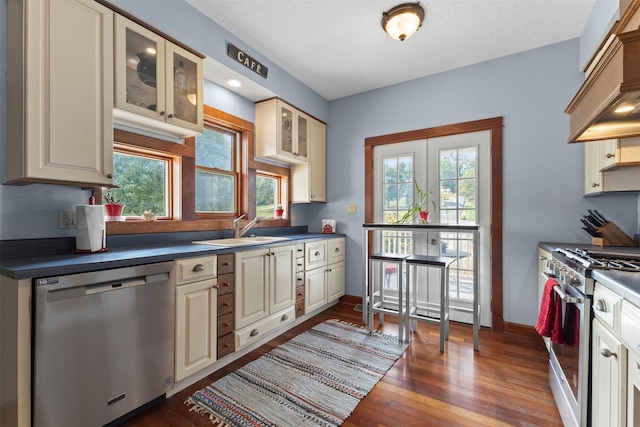 1905 W Olive St, Marshalltown, IA 50158 - kitchen featuring appliances with stainless steel finishes, a sink, dark countertops, cream cabinetry, and custom range hood