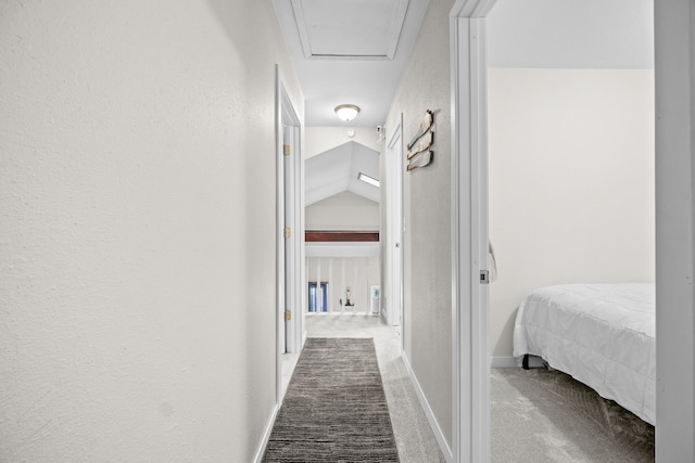 hallway with carpet floors, lofted ceiling, a textured wall, attic access, and baseboards