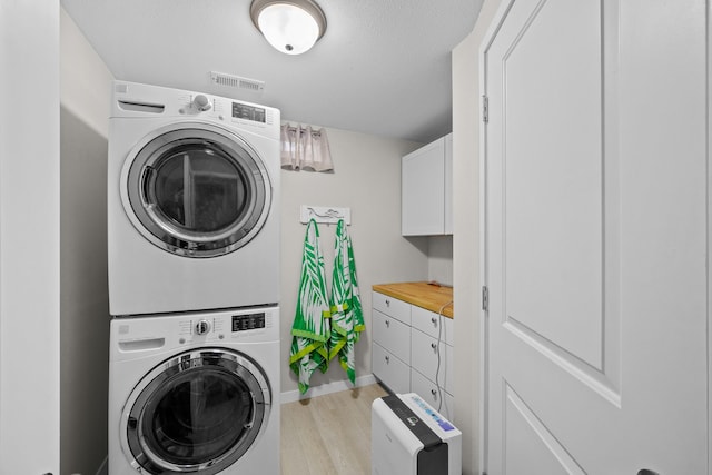 laundry room featuring laundry area, visible vents, baseboards, stacked washer / drying machine, and light wood-type flooring