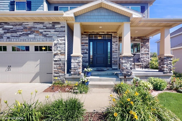 doorway to property with an attached garage, stone siding, and covered porch