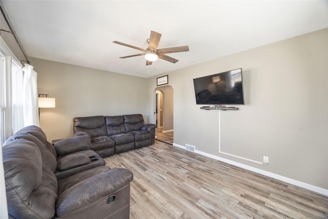 living area with arched walkways, ceiling fan, visible vents, baseboards, and light wood-style floors