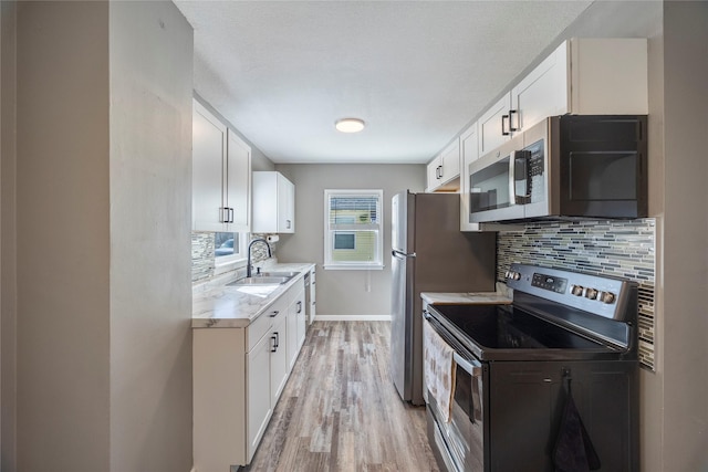 kitchen featuring stainless steel appliances, decorative backsplash, light wood-style floors, white cabinets, and a sink