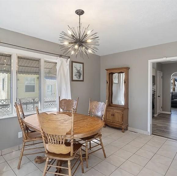 dining room featuring baseboards, a healthy amount of sunlight, light tile patterned flooring, and an inviting chandelier