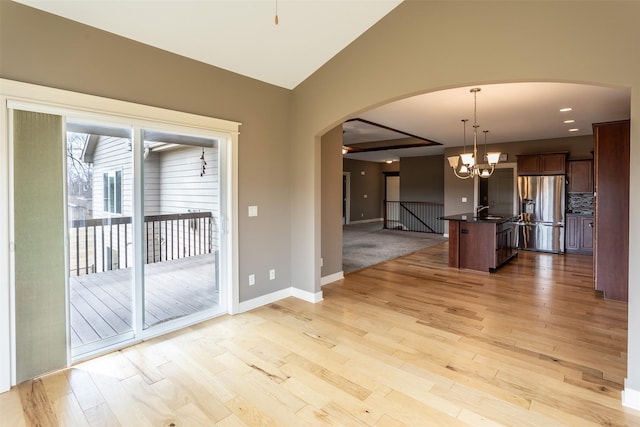 empty room with arched walkways, light wood finished floors, an inviting chandelier, vaulted ceiling, and baseboards