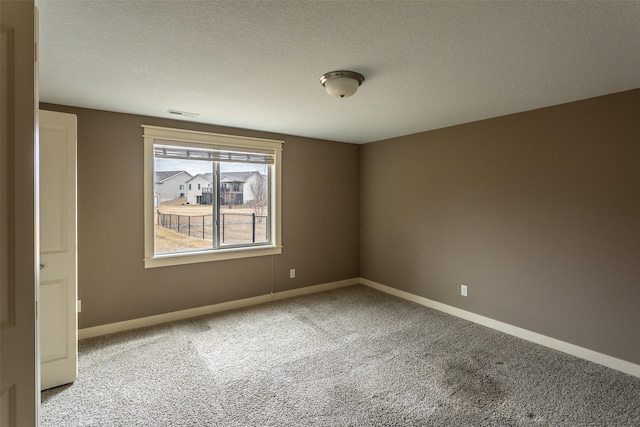 empty room with carpet floors, visible vents, a textured ceiling, and baseboards