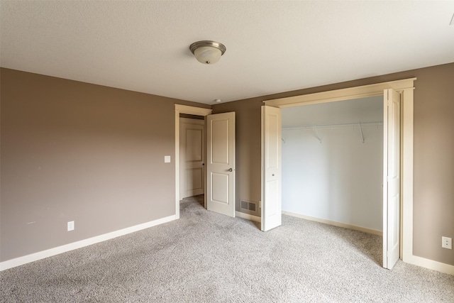 unfurnished bedroom with a textured ceiling, light carpet, visible vents, baseboards, and a closet