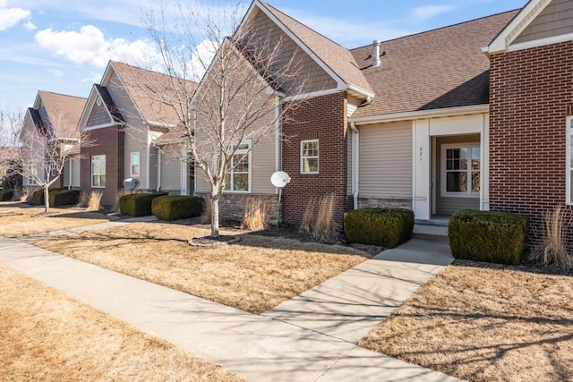 view of front of home featuring a shingled roof, stone siding, and brick siding