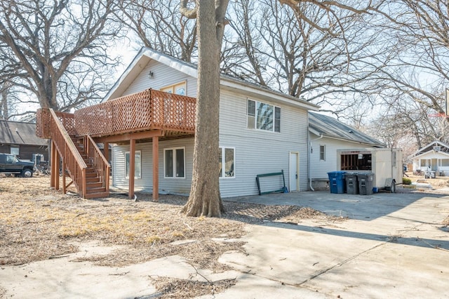 rear view of property with driveway, an attached garage, stairway, and a wooden deck