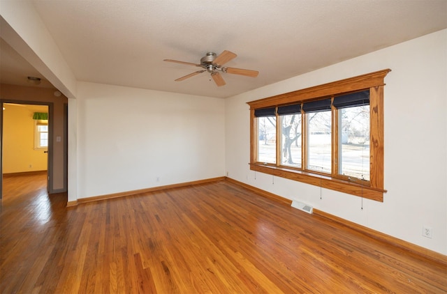 unfurnished room with baseboards, wood finished floors, visible vents, and a healthy amount of sunlight