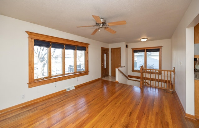 unfurnished room with baseboards, light wood-style flooring, visible vents, and a textured ceiling