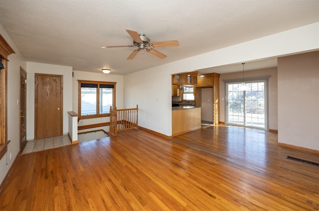 unfurnished living room with a textured ceiling, a wealth of natural light, wood finished floors, and visible vents