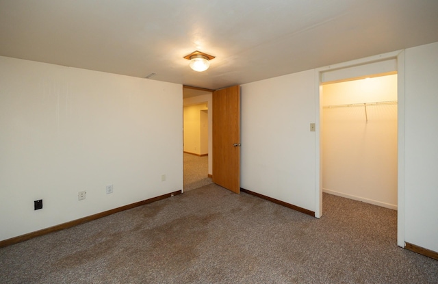 unfurnished bedroom featuring a closet, a spacious closet, baseboards, and carpet flooring