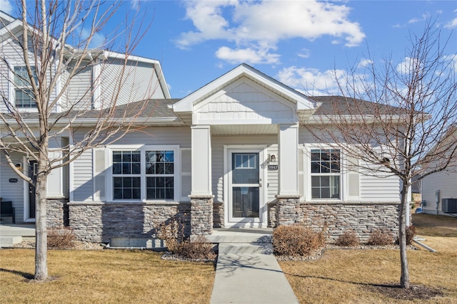 view of front facade featuring stone siding, a shingled roof, a front lawn, and central AC