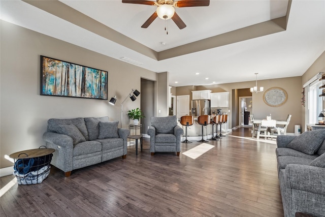 living area featuring baseboards, visible vents, a raised ceiling, dark wood finished floors, and ceiling fan