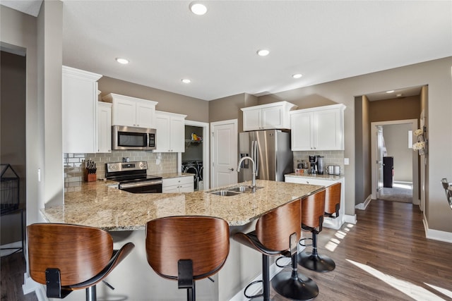 kitchen with light stone counters, dark wood-style flooring, stainless steel appliances, a sink, and a peninsula