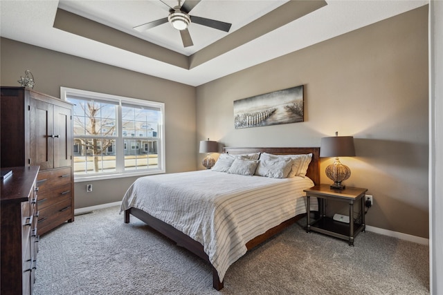 carpeted bedroom with baseboards, a tray ceiling, and a ceiling fan