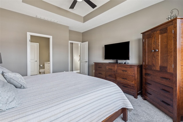 bedroom with light carpet, visible vents, ceiling fan, ensuite bathroom, and a tray ceiling