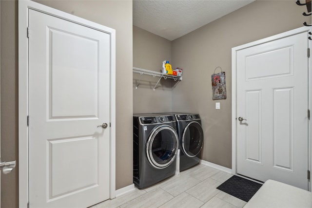 clothes washing area featuring a textured ceiling, laundry area, separate washer and dryer, and baseboards