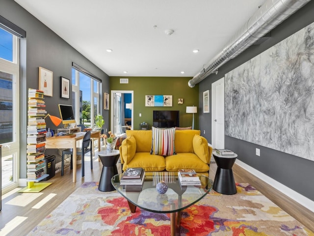 living area featuring wood finished floors, an accent wall, baseboards, and recessed lighting