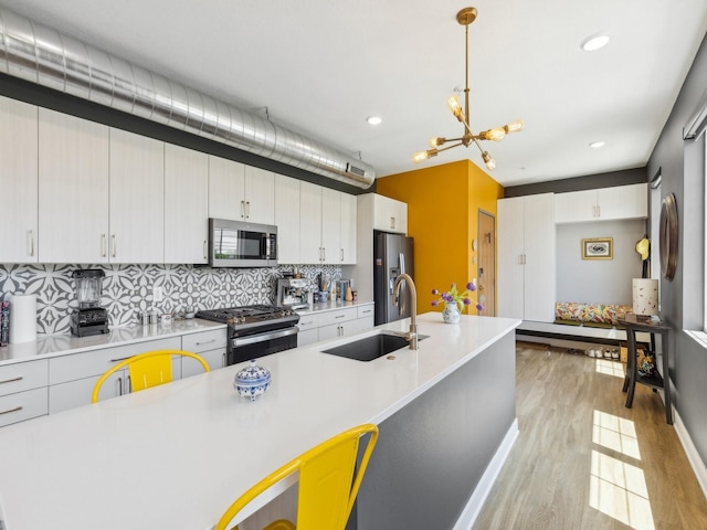 kitchen with stainless steel appliances, a sink, light countertops, light wood-type flooring, and backsplash