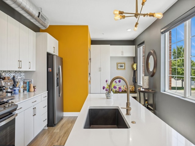 450 SW 7th St Unit 210, Des Moines, IA 50309 - kitchen with appliances with stainless steel finishes, a sink, a chandelier, light wood finished floors, and light countertops