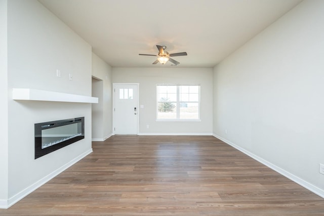 unfurnished living room featuring a ceiling fan, a glass covered fireplace, baseboards, and wood finished floors