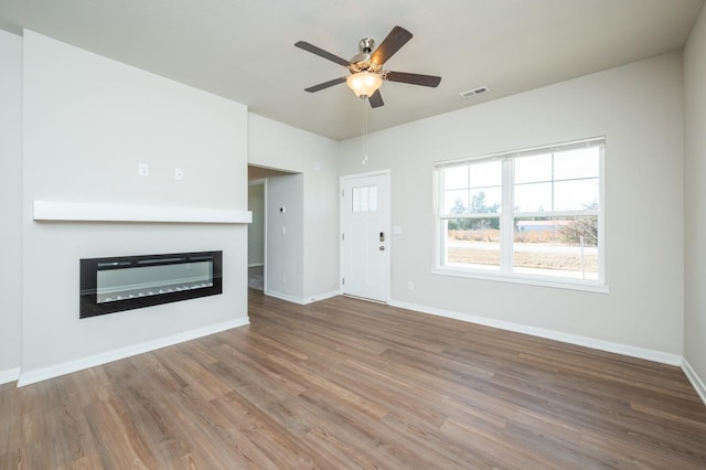 unfurnished living room featuring baseboards, visible vents, a glass covered fireplace, ceiling fan, and wood finished floors