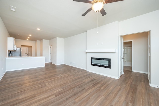 unfurnished living room featuring a sink, visible vents, wood finished floors, and a glass covered fireplace