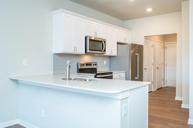 kitchen with stainless steel appliances, a peninsula, wood finished floors, a sink, and tasteful backsplash