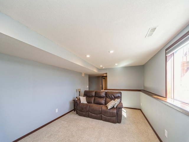 living area featuring light carpet, visible vents, baseboards, and a textured ceiling