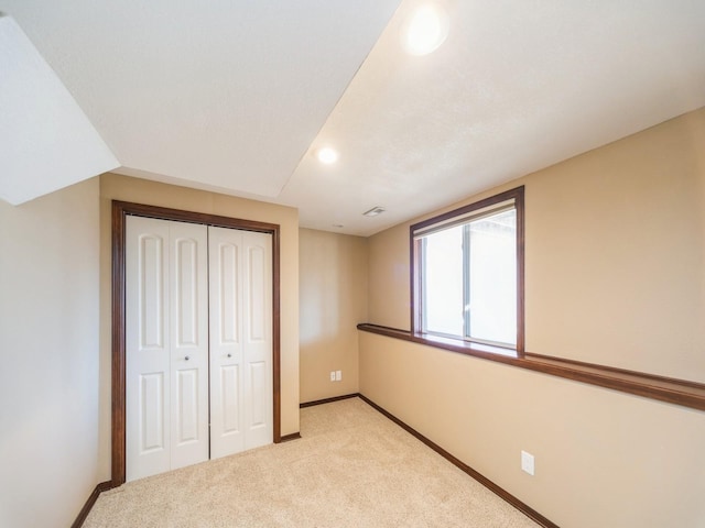 unfurnished bedroom featuring baseboards, a closet, visible vents, and light colored carpet