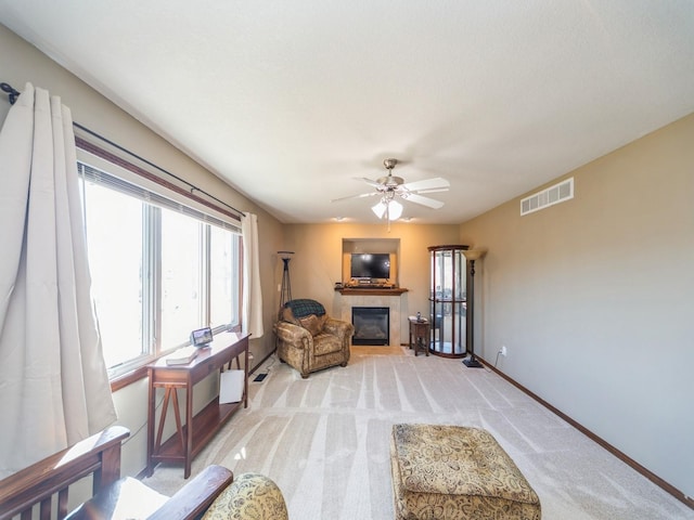 sitting room featuring baseboards, visible vents, a ceiling fan, a tile fireplace, and light colored carpet