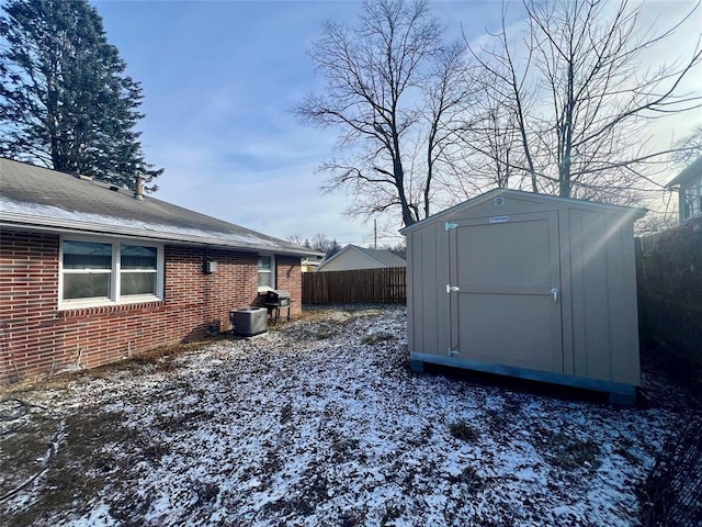 snowy yard with a storage shed, an outbuilding, and fence