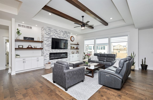 living room with dark wood-type flooring, a tray ceiling, beam ceiling, and a stone fireplace