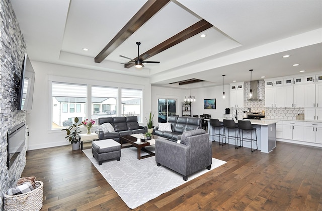 living room with dark wood-style floors, a stone fireplace, beam ceiling, and recessed lighting