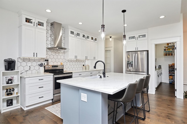 kitchen with a center island with sink, dark wood-style floors, wall chimney exhaust hood, stainless steel appliances, and a sink