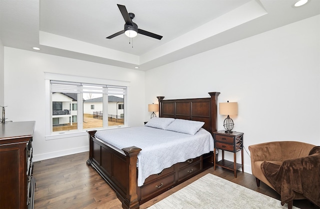 bedroom featuring dark wood-style floors, a tray ceiling, and baseboards