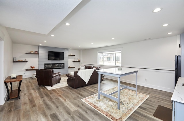 living room featuring a large fireplace, baseboards, wood finished floors, and recessed lighting