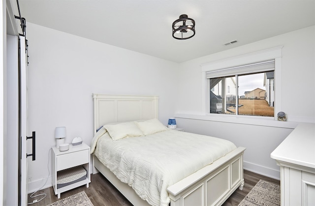 bedroom featuring a barn door, dark wood-style flooring, and visible vents