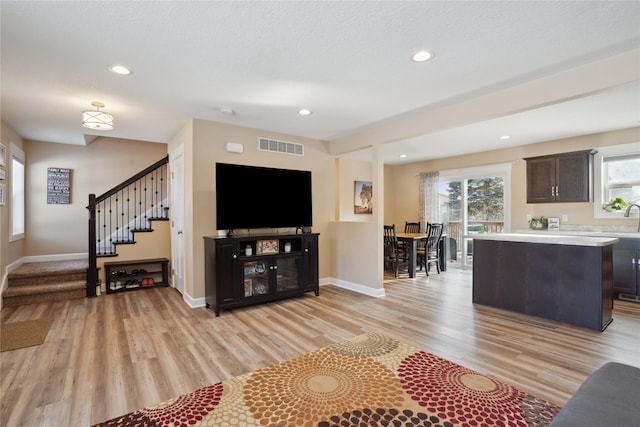 living room featuring visible vents, light wood-style flooring, baseboards, and stairs