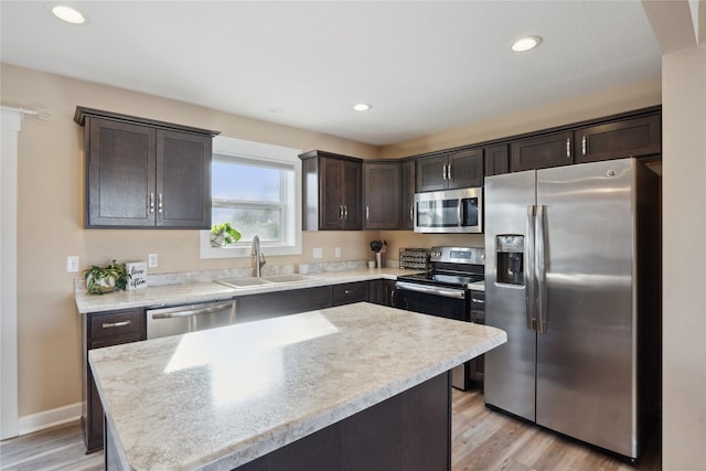 kitchen with appliances with stainless steel finishes, a sink, light wood-style flooring, and dark brown cabinetry