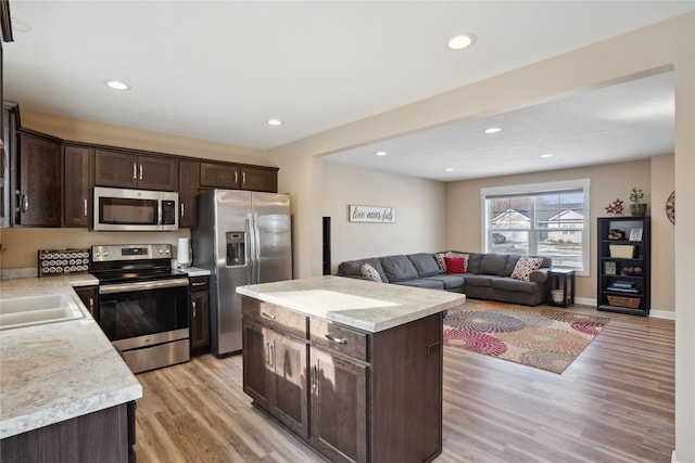 kitchen featuring a kitchen island, appliances with stainless steel finishes, light countertops, dark brown cabinets, and light wood-type flooring