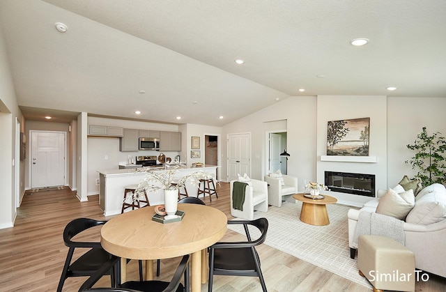 dining area with light wood-style floors, vaulted ceiling, a glass covered fireplace, and baseboards