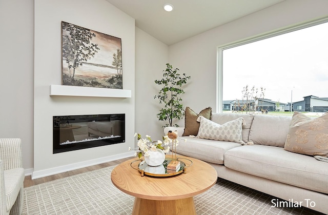 living room featuring vaulted ceiling, wood finished floors, a glass covered fireplace, baseboards, and recessed lighting