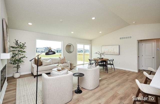 living room with light wood-style flooring, visible vents, vaulted ceiling, and baseboards