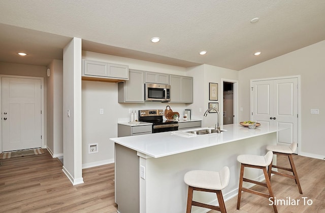 kitchen with a sink, gray cabinets, stainless steel appliances, light wood-style flooring, and baseboards